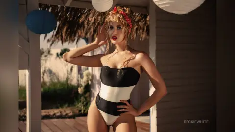 Blonde woman in a black and white striped swimsuit posing on a sunny wooden deck.