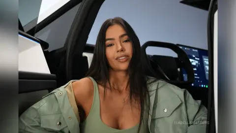 Smiling brunette woman in a sage green outfit sitting inside a modern car interior.