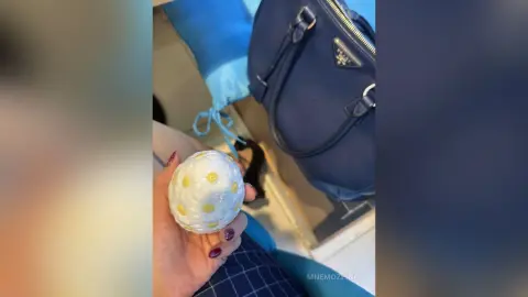 Hand holding a white and yellow patterned decorative egg near a navy blue designer handbag.