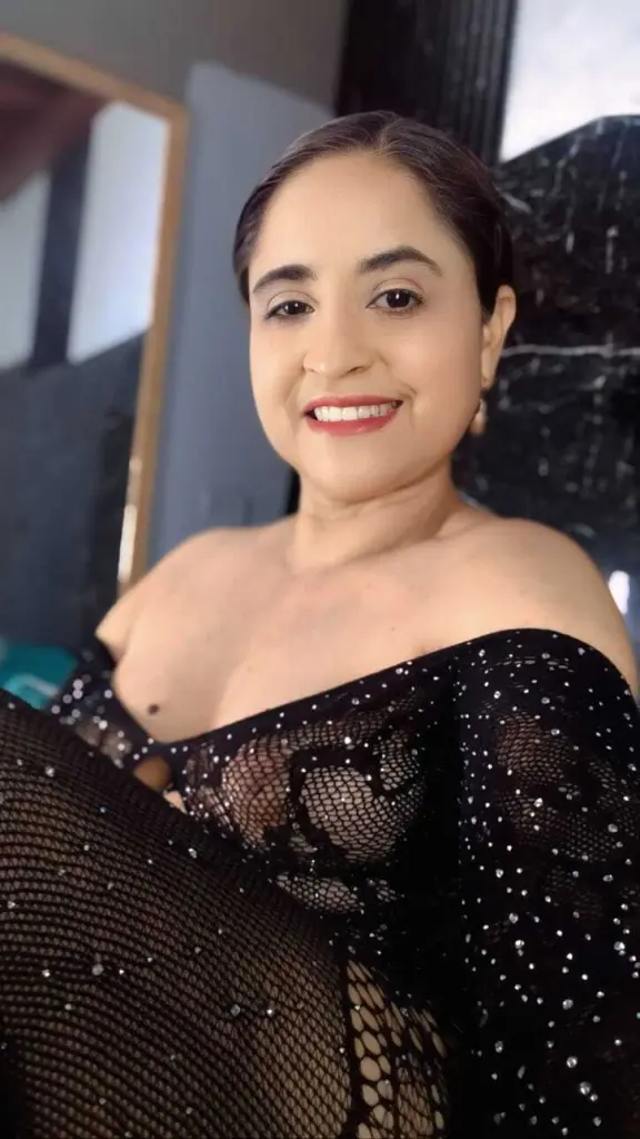 Smiling woman with dark hair and red lipstick wearing elegant silver earrings in a bright indoor setting.