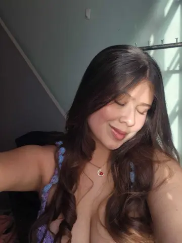 Smiling woman with long wavy hair wearing a purple crochet top in soft natural sunlight.