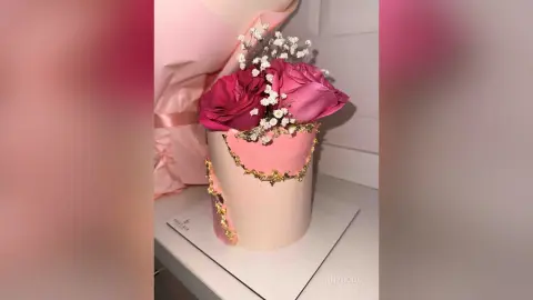 Elegant pink floral cake decorated with gold accents and fresh roses on a white base.