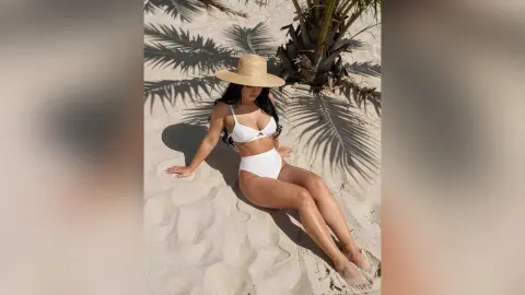 Woman in white bikini and straw hat relaxing on a sunny tropical beach sand.