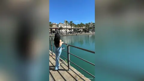 Woman in light blue jeans standing by a scenic canal overlooking historic European architecture on a sunny day.