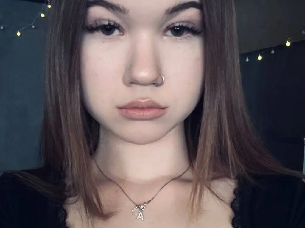 Close-up portrait of a young woman with long brown hair and a nose ring in a moody, dimly lit room.