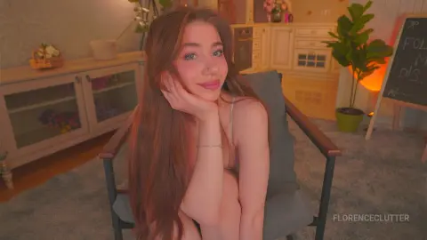Smiling young woman with long brown hair relaxing in a cozy, warm-lit living room setting.