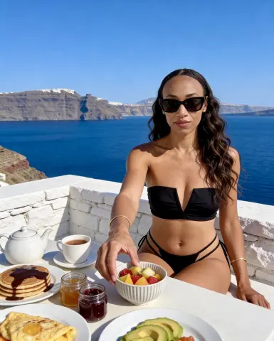 MistressJacksonMonroe sits at an outdoor table by the ocean wearing a black bikini and sunglasses.