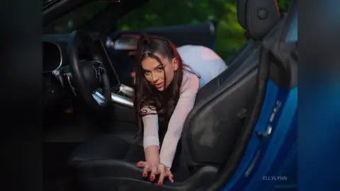 Stylish woman in a white long-sleeve top sitting in a blue car interior with a moody, cinematic aesthetic.