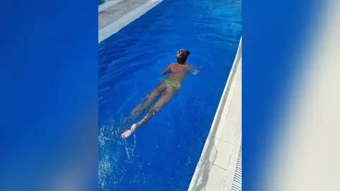 Young woman in a green bikini swimming in a bright blue outdoor pool on a sunny summer day.