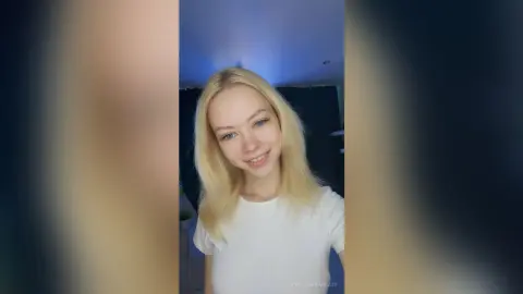 Smiling blonde woman in a white t-shirt posing in a bright indoor setting with a cheerful mood.