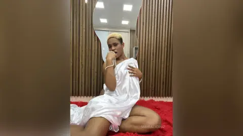 Young woman in a white satin dress sitting on a red shag rug in a modern room with wood slat walls.