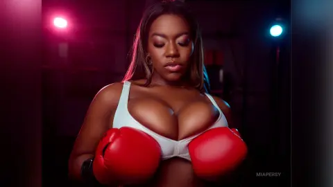 Curvy woman in a white sports bra wearing red boxing gloves in a moody, dimly lit gym setting.