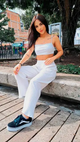 Young woman in white ribbed crop top and lounge pants sitting outdoors on a sunny day.