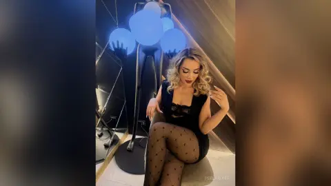 Glamorous woman in a black lace outfit and patterned tights posing by a modern blue orb floor lamp.