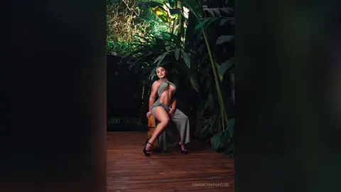 Elegant woman in a sage green halter jumpsuit posing in a lush tropical garden setting.