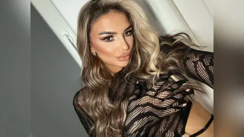 Anastasia poses in a black lace mesh top, showing her long wavy blonde hair and heavy eye makeup.