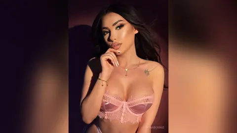 Glamorous woman in pink lace lingerie posing with soft lighting in a moody, elegant studio setting.