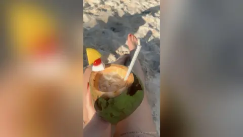 Refreshing coconut cocktail with a straw and fruit garnish held on a sunny tropical beach vacation.