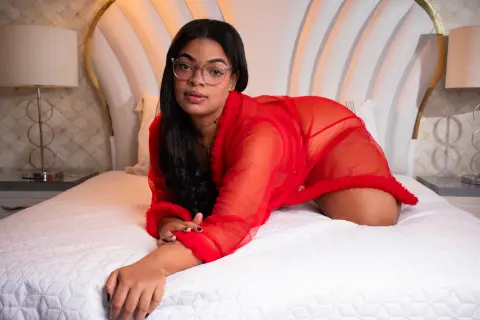Young woman in a red sheer robe relaxing on a white bed in a bright, elegant bedroom.