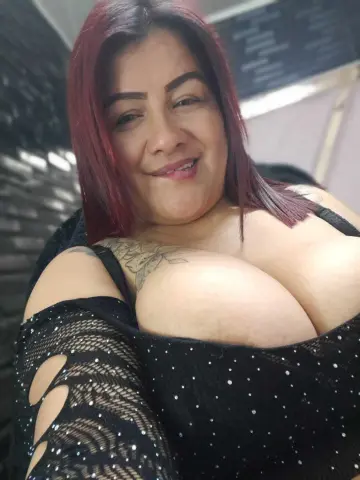 ScarlettSexRs smiles while wearing a black sparkly top that shows off her large breasts and chest tattoo.