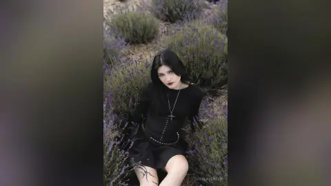 Gothic woman in a black dress and cross necklace sitting in a dreamy purple lavender field.