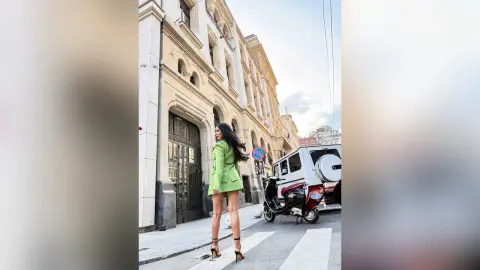 NicoleBella stands on a city street wearing a short lime green jacket and matching skirt with black high heels.