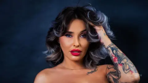 Beautiful woman with wavy grey hair and red lipstick posing against a dark studio background.