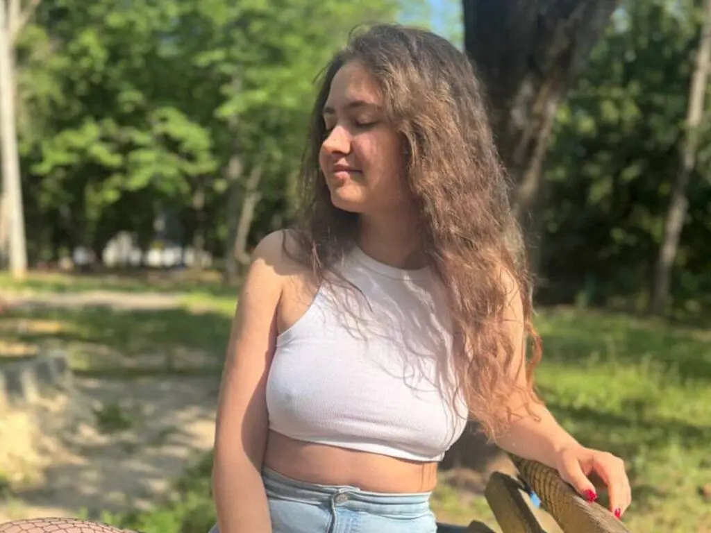 Young woman in a white crop top relaxing outdoors in a sunny park setting.