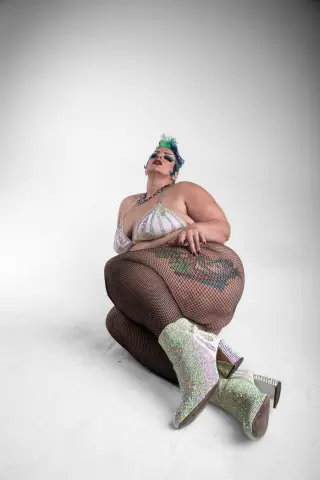 Glamorous plus-size woman in a sparkly silver bikini and fishnets posing confidently against a white background.