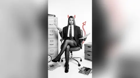 AvaBronX — AvaBronX sits in an office chair wearing a black blazer, white shirt, tie, and skirt with red devil horns edited onto her head.