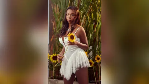 Beautiful woman in a white lace romper holding a sunflower in a lush tropical garden setting.