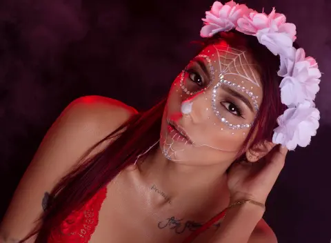 Woman in red lace with skull face paint and white flower crown in moody red lighting.