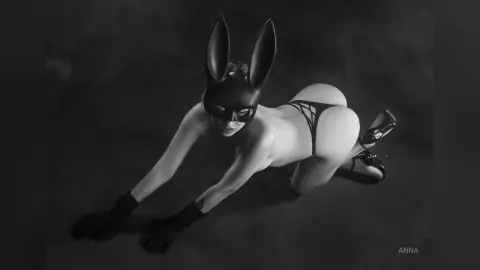 Woman in black bunny mask and lingerie posing on a dark floor in a moody black and white portrait.