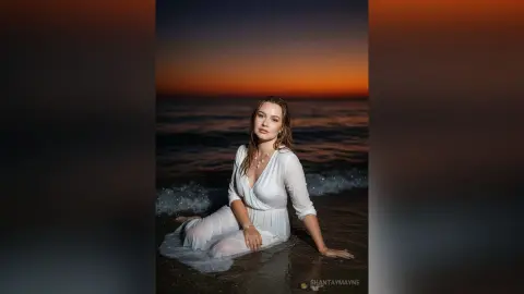 ShantayMayne sits in the shallow ocean waves wearing a white sheer dress at sunset.