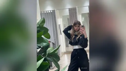 Stylish young woman in a black crop top and joggers taking a mirror selfie in a modern clothing boutique.