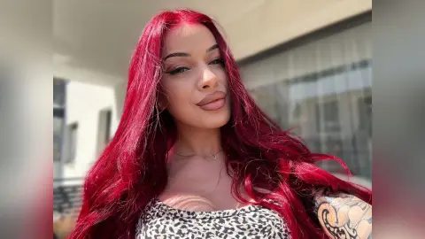 AriaVex smiles with long red hair while wearing a leopard print top outdoors.