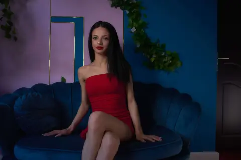 Elegant woman in a red strapless dress sitting on a blue velvet sofa in a moody, stylish room.