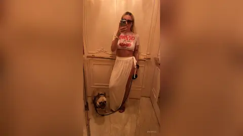 AmaFox — Blonde woman in a white cherry graphic crop top and long skirt taking a mirror selfie with her dog.