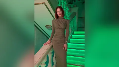 SheraRich poses in a tight, long-sleeved olive dress while standing on a glowing green staircase.