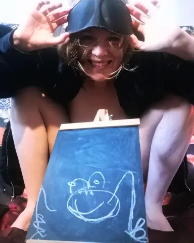ChillBillie smiles while wearing a black sleep mask and sitting behind a small chalkboard with a drawing of a frog.