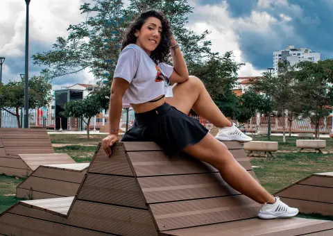 Smiling woman in a white t-shirt and black skirt sitting on wooden stairs in a sunny park.