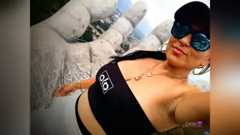 Smiling woman in black crop top and sunglasses posing in front of a large white stone statue.