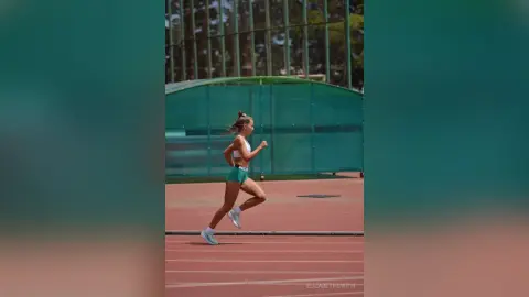 Athletic woman in white sports bra and teal shorts running on a track during a sunny outdoor workout.