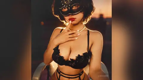 Mysterious woman in black lace lingerie and masquerade mask posing during a golden hour sunset.
