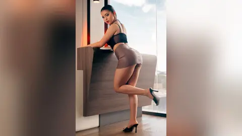 VickyPortman poses against a wooden desk wearing a black bra and a short brown skirt.