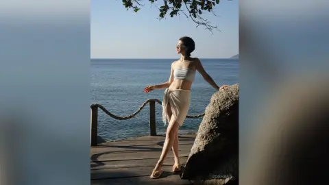 Stylish woman in a white bikini and sarong relaxing on a wooden pier by the sunny blue ocean.