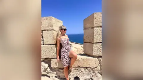 KaylaBryan poses in a zebra print dress against a stone wall with the blue ocean in the background.