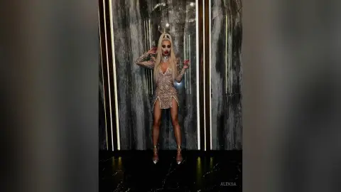 Glamorous blonde woman in a sparkling sequin mini dress posing in a luxury marble interior.