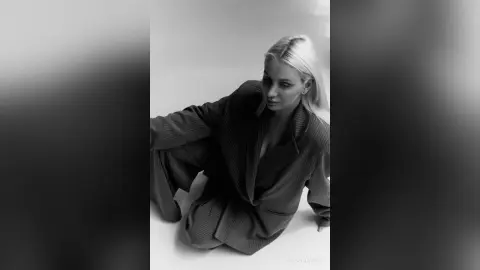 Elegant woman in a stylish oversized blazer posing in a minimalist studio setting, black and white aesthetic.