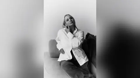 Elegant woman in a white button-down shirt relaxing on a sofa in a minimalist black and white portrait.